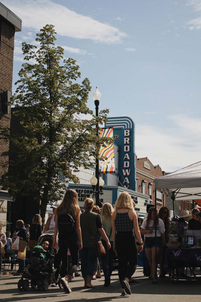 A crowd walking down Broadway Avenue in Saskatoon, with the Broadway Theatre sign visible.